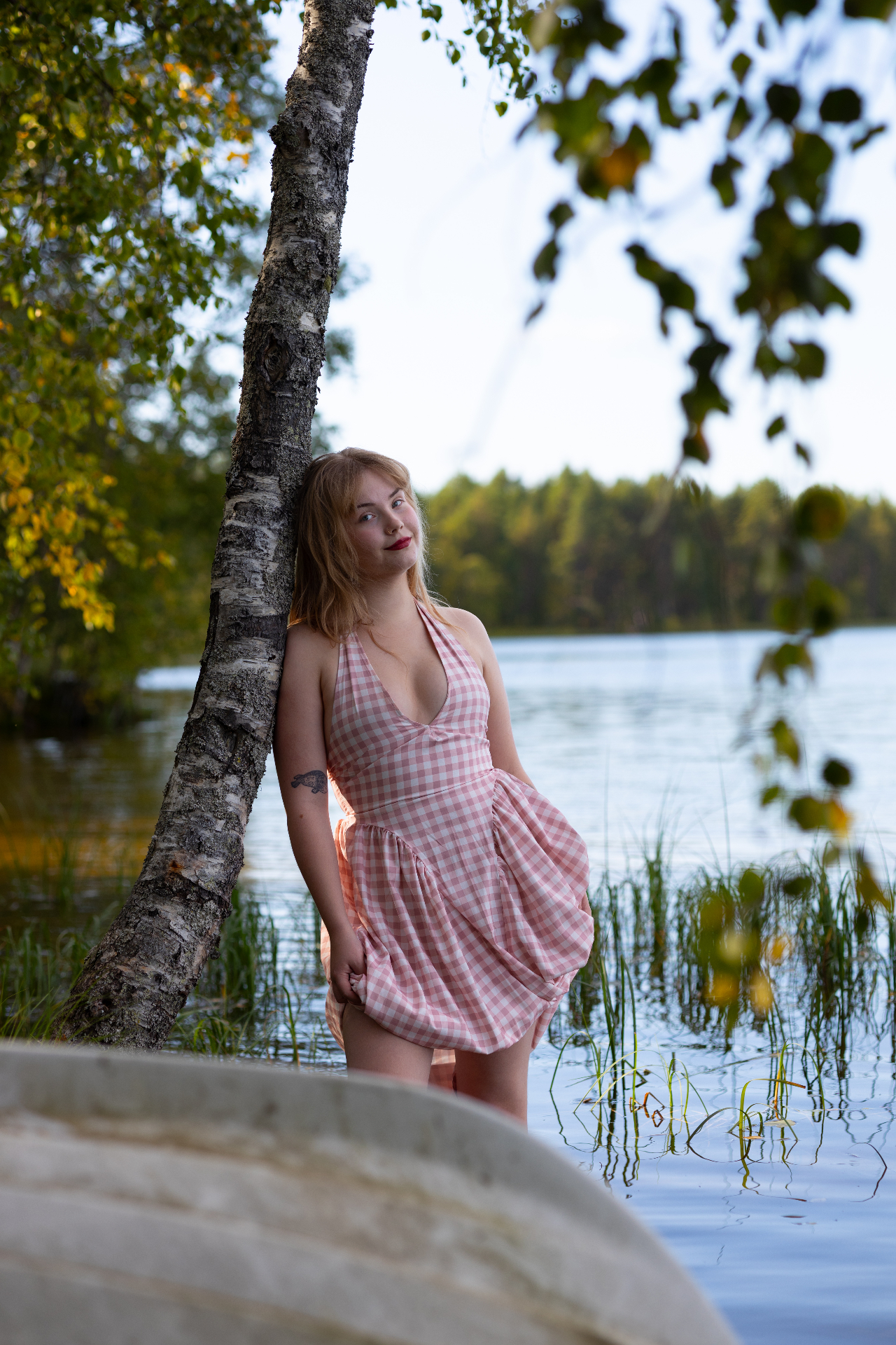 Young woman in a pink gingham dress by a birch tree at the lake