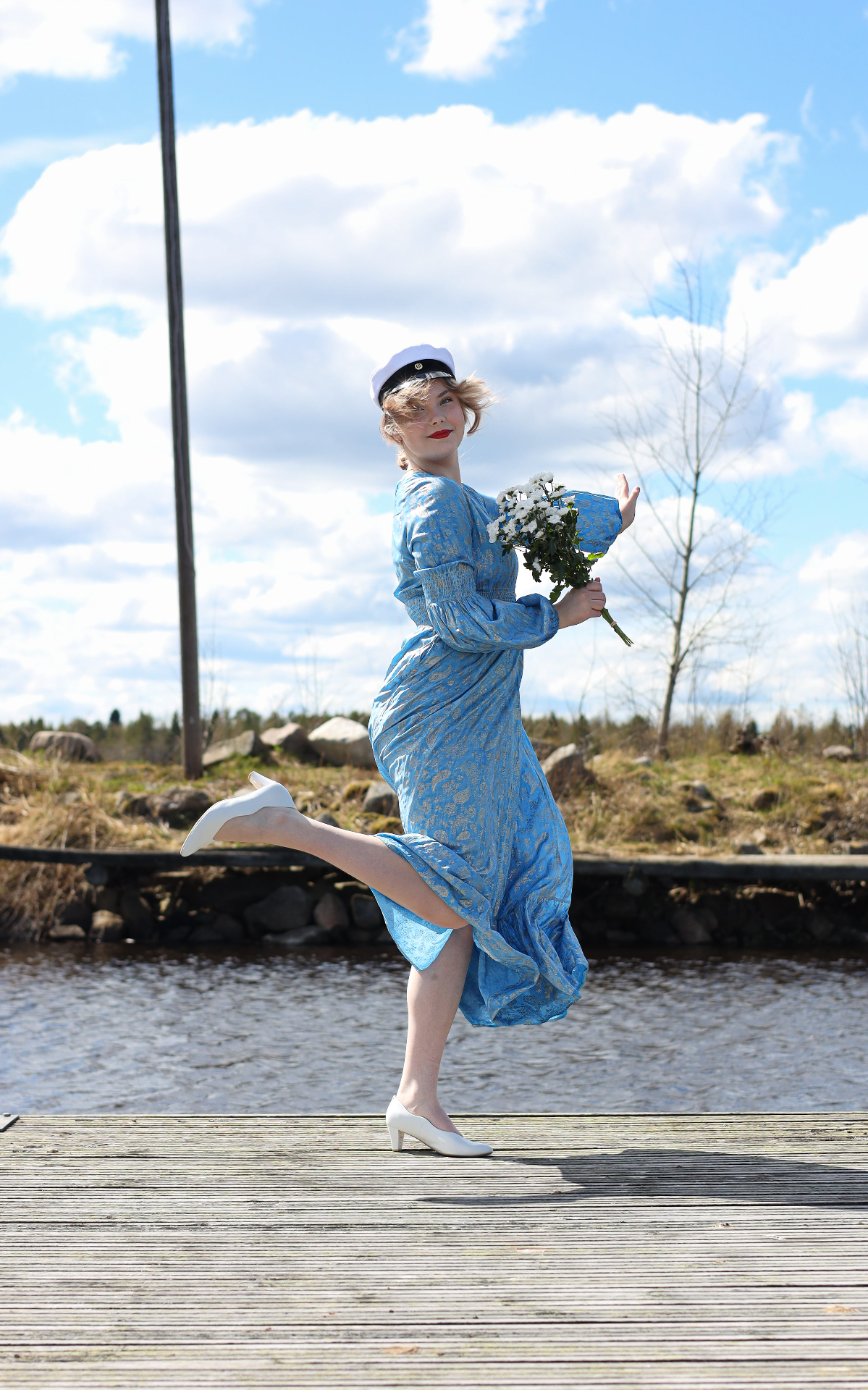 Graduate in student cap dancing on a lakeside dock